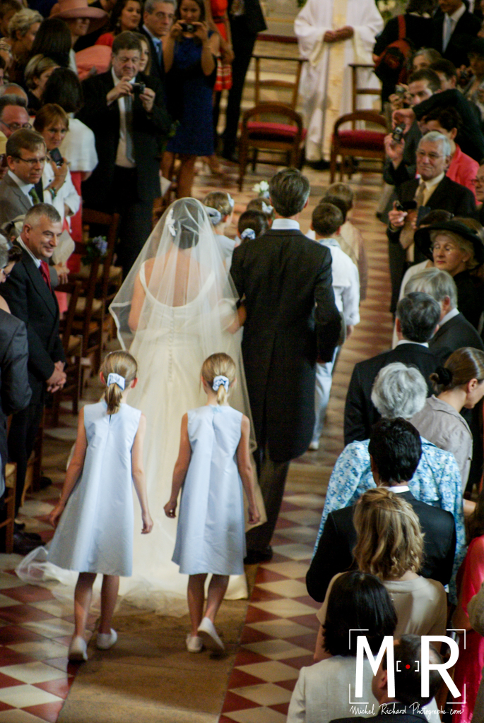 la mariée de dos aux bras de son père avance avec le cortège des enfants d'honneur. Belle lumière sur le voile et les robes. cérémonie de la messe de mariage.