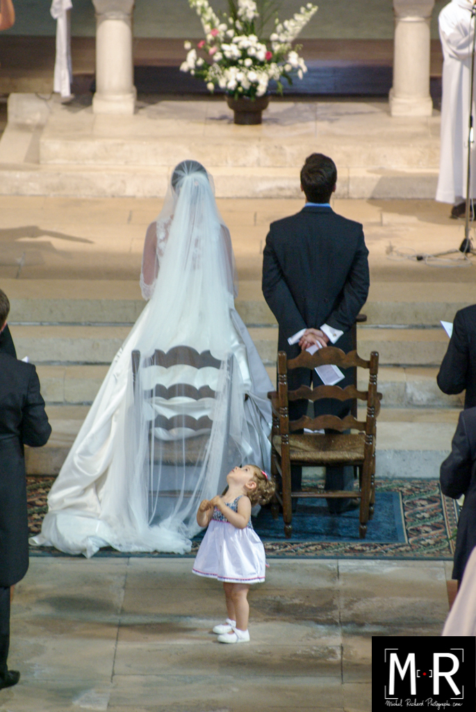 un enfant - une petite fille d'honneur regarde en l'air derrière les mariés à l'église pendant la cérémonie de la messe du mariage