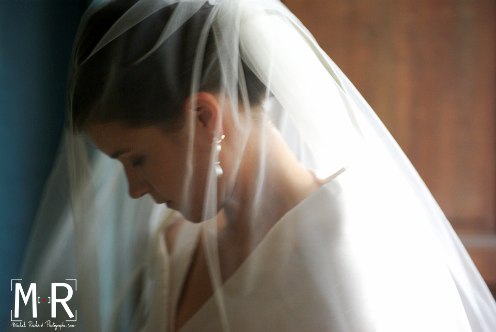 la mariée est en contrejour sous son voile à l'entrée de l'église pour la cérémonie de mariage