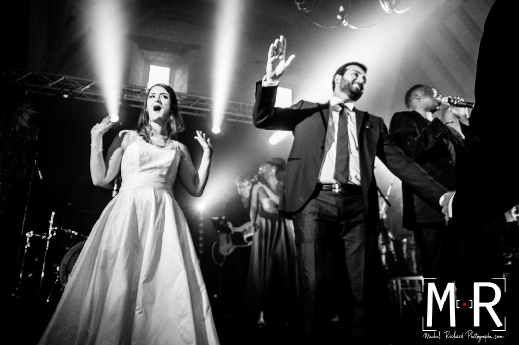 les mariés dansent sur scène sous les projecteurs en noir et blanc.
