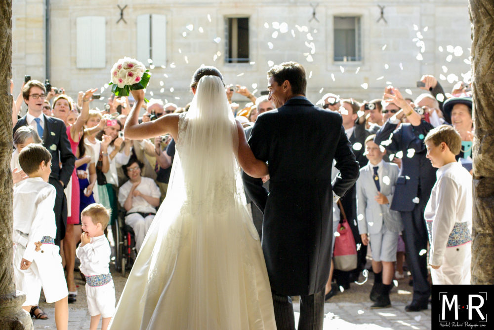 les mariés de dos à la sortie de l'église pour leur cérémonie de mariage, après la messe, sous la pluie de pe pétales de roses
